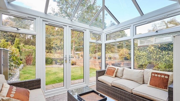 A conservatory with a glass roof, wicker furniture, and a view of a garden. - Host Stay The Station Cottage (Rowlands Gill)