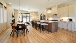 A modern kitchen with a central island, bar stools, and a dining area with a wooden table and chairs.