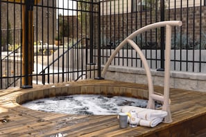 A hot tub with a wooden deck, a metal railing, and a towel rack.