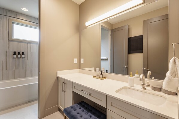 A modern bathroom with a large mirror, a bathtub, and a vanity with a sink and drawers.