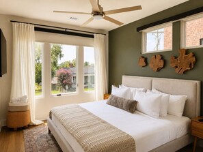 A bedroom with a bed, a ceiling fan, a window with curtains, and a view of the outside.