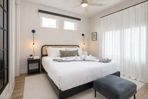 Une chambre moderne avec un grand lit, des tables de chevet, un ventilateur de plafond et une fenêtre avec des rideaux.