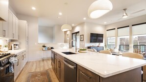 A modern kitchen with a large island, built-in appliances, pendant lighting, and a view to the outside.