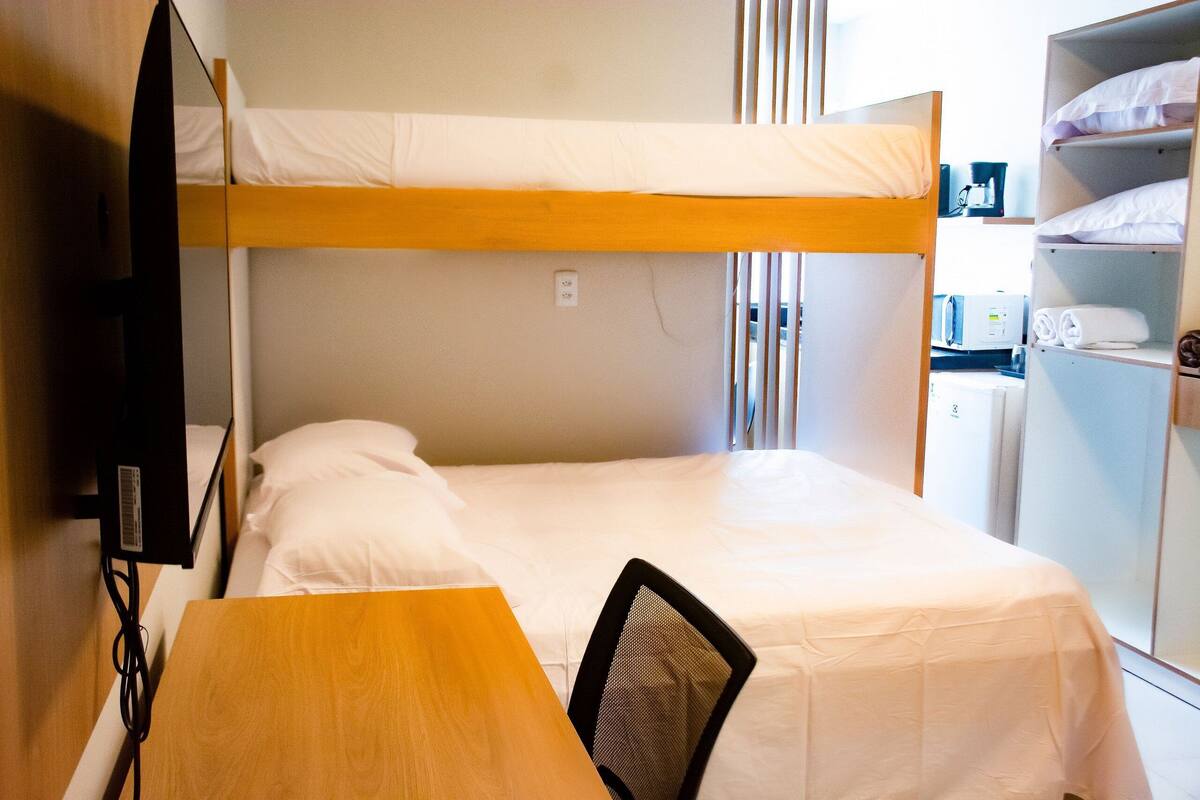 A bunk bed with a desk and chair, a television, and a wardrobe with shelves.