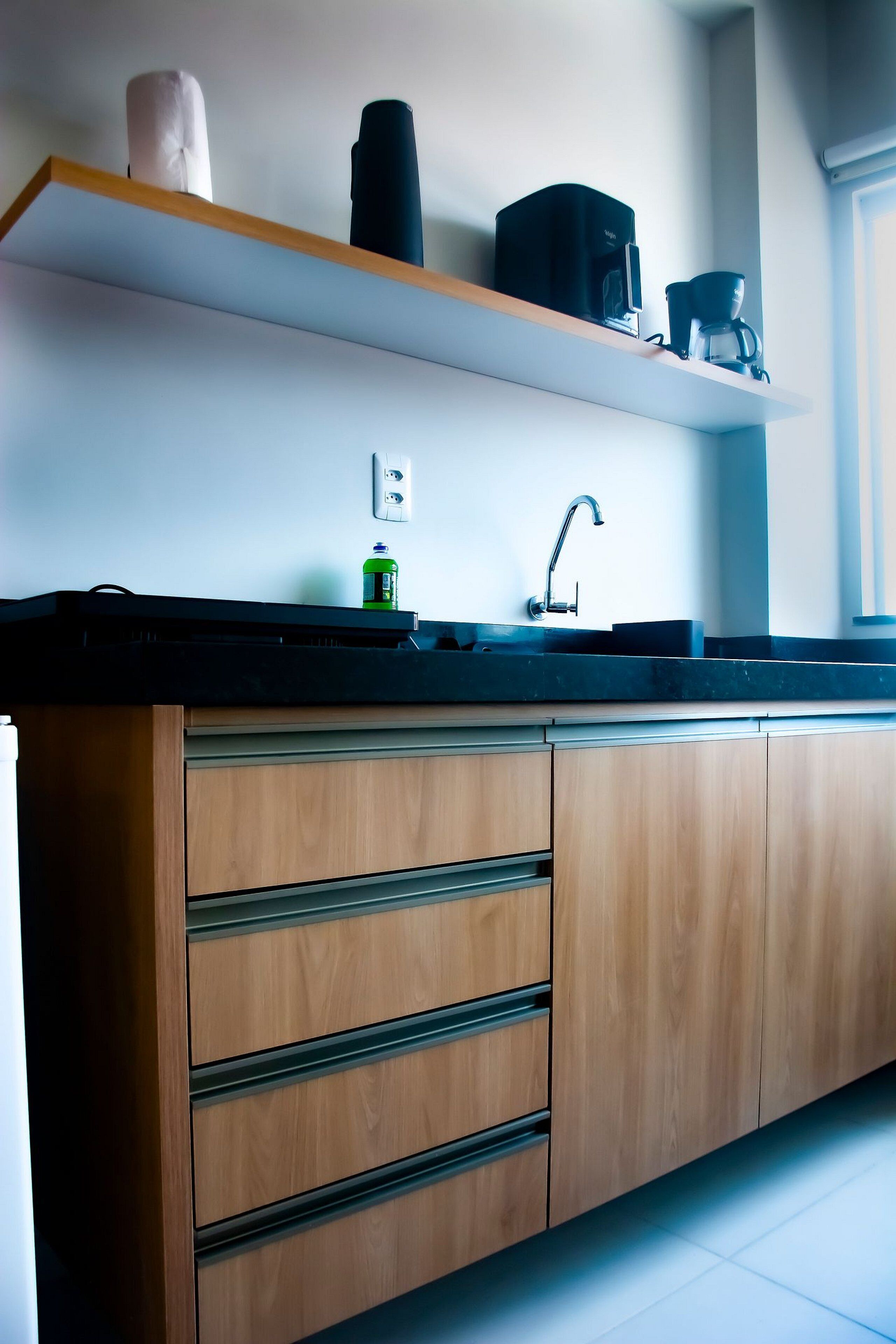 A modern kitchen with wooden cabinets, a black countertop, a coffee machine, and a sink.
