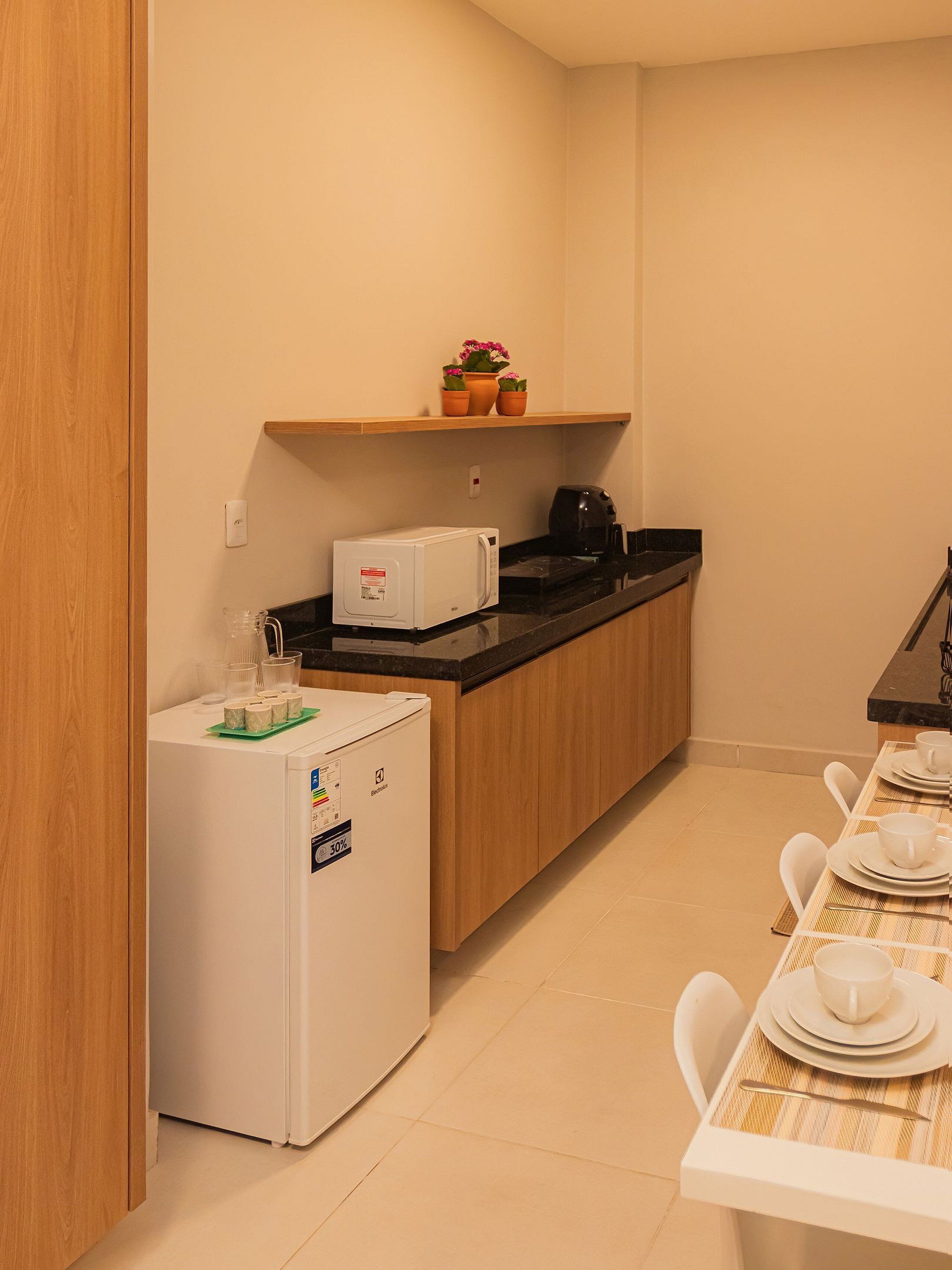 Cocina compacta con refrigerador, microondas, cafetera y un pequeño estante con plantas en macetas.