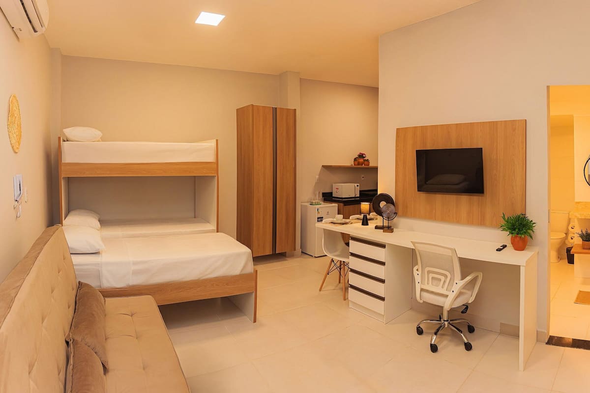 A compact bedroom with a bunk bed, a desk with a chair, a small kitchenette, and a bathroom.
