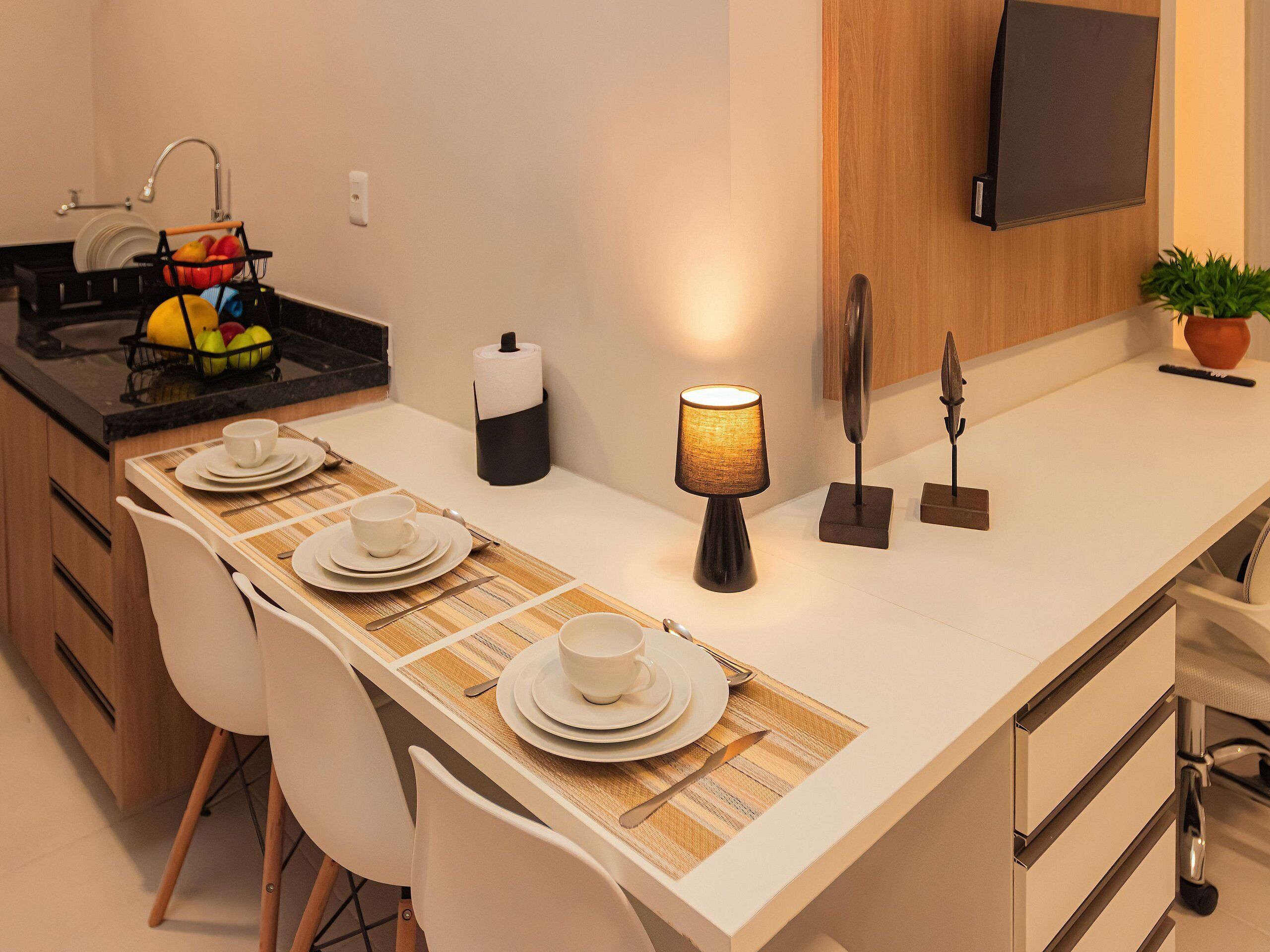 Una cocina moderna con una larga mesa de comedor preparada para cuatro personas, estufa empotrada y un televisor de pantalla plana montado en la pared.
