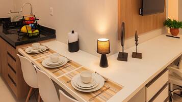 Una cocina moderna con una larga mesa de comedor preparada para cuatro personas, estufa empotrada y un televisor de pantalla plana montado en la pared.