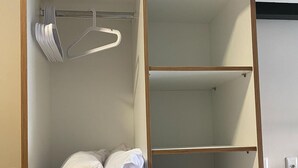 Un placard avec deux étagères, l’une servant à ranger des serviettes pliées et l’autre des vêtements suspendus.