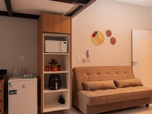 A compact living space with a sofa, a microwave, a refrigerator, and a shelf with potted plants. - HN Pariquis (Belém)