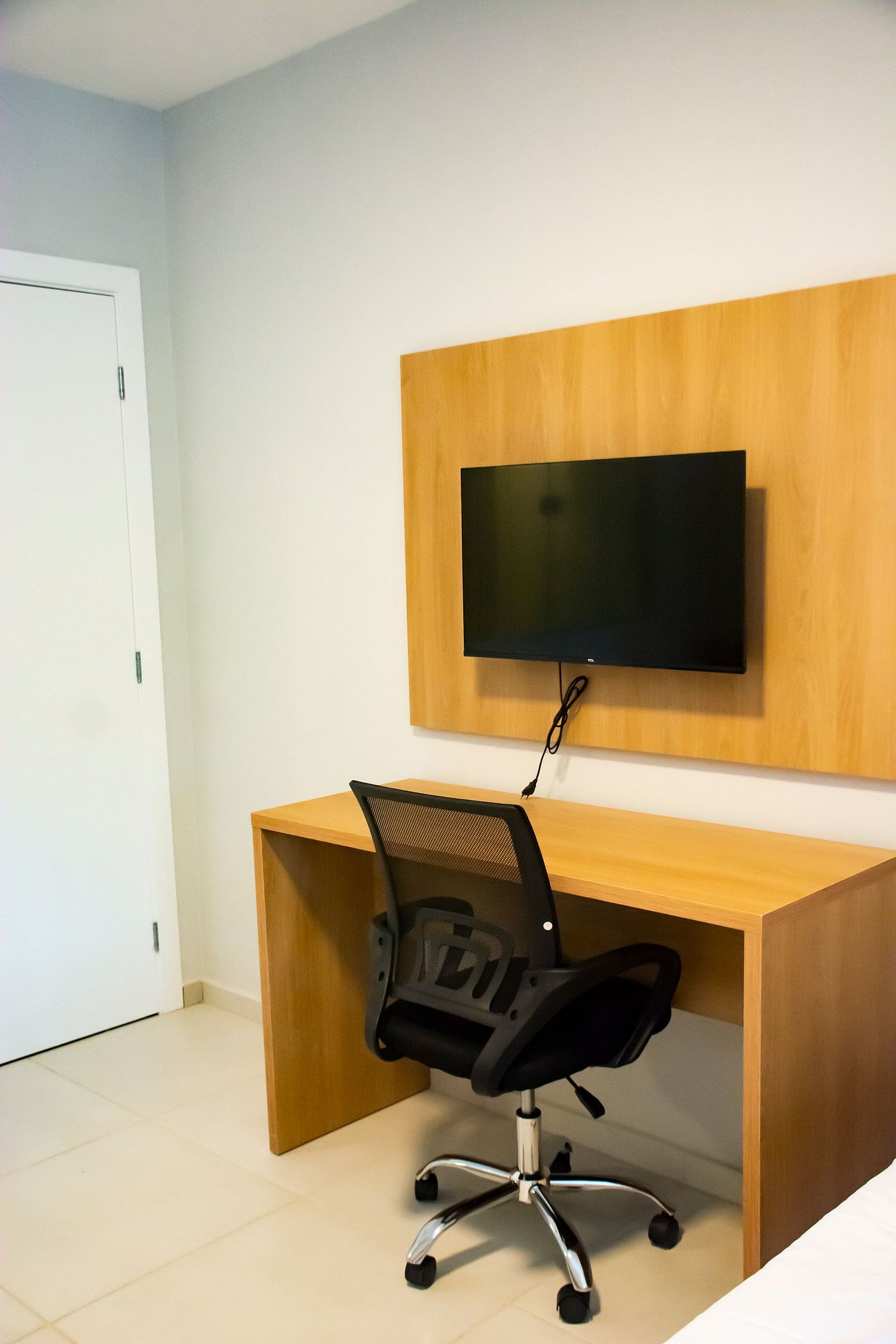 Een kamer met een houten bureau, een zwarte bureaustoel en een wandgemonteerde flatscreen-tv.