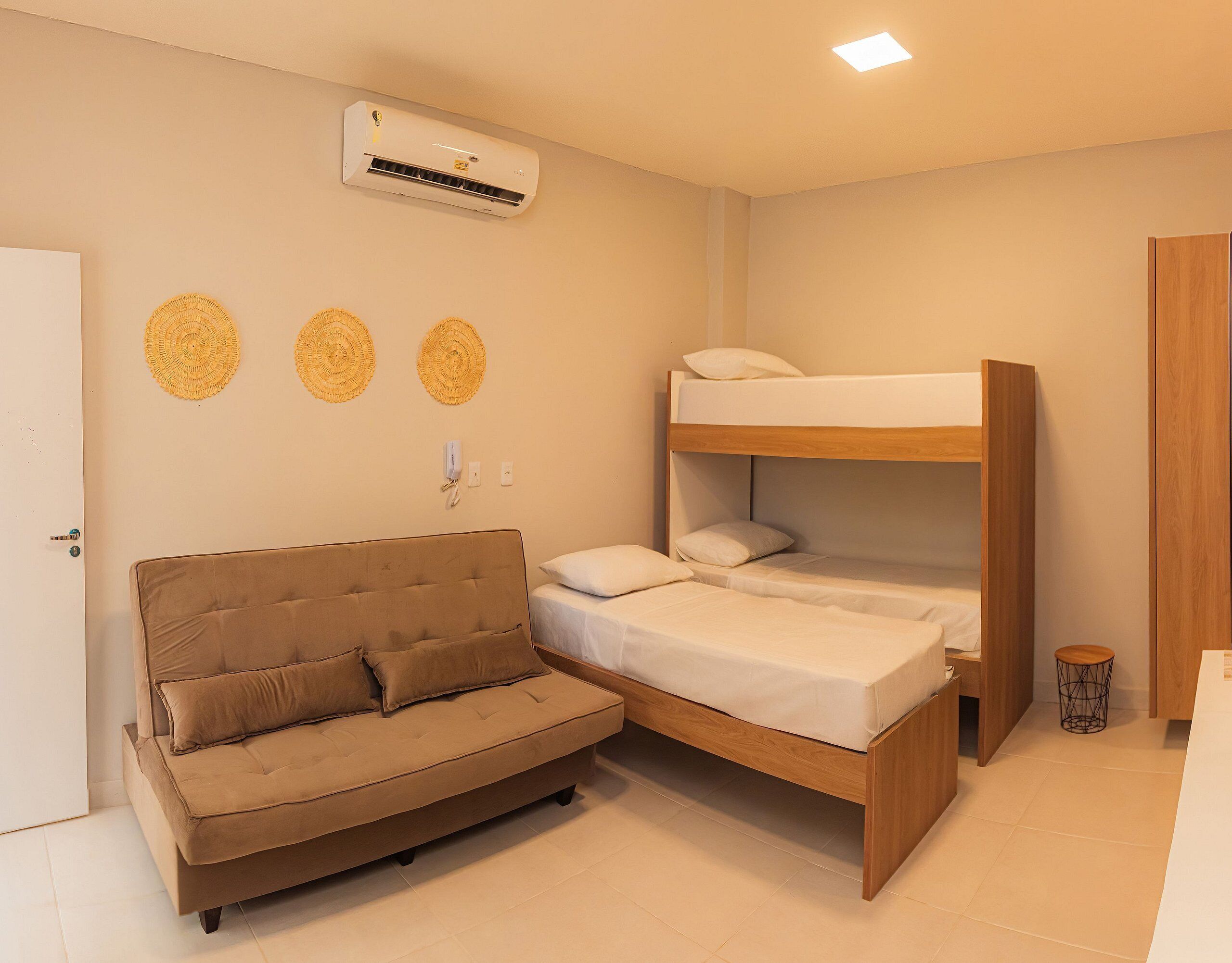 A compact room with a bunk bed, a sofa, and an air conditioning unit on the wall.