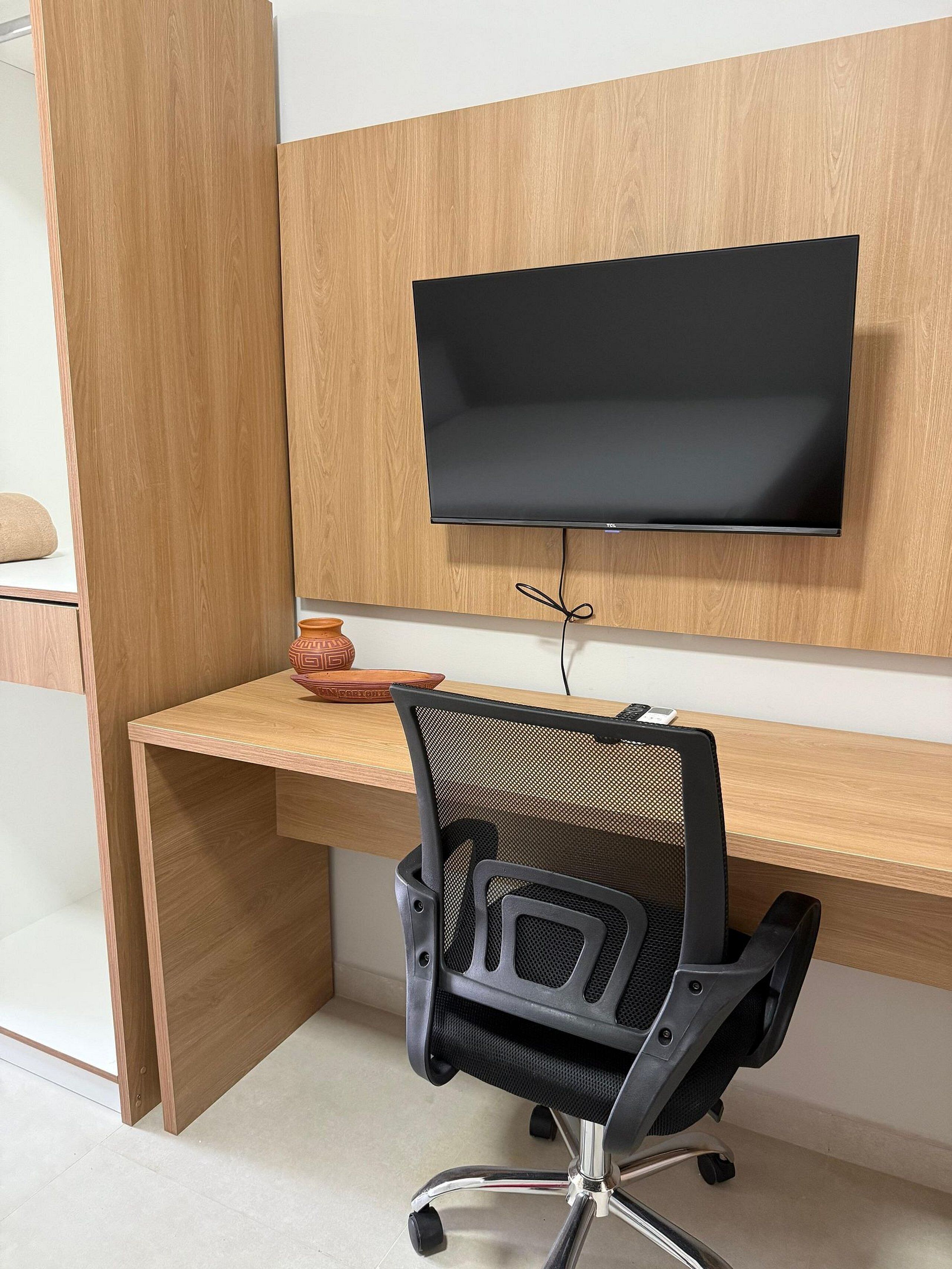 A modern office space with a wooden desk, a black office chair, and a mounted flat-screen TV.