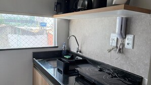 Une cuisine compacte avec un plan de travail noir, des placards en bois, une machine à café, un téléphone et une fenêtre donnant sur des immeubles.