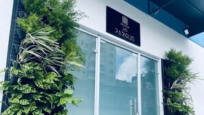 Η είσοδος ενός ξενοδοχείου με μια γυάλινη πόρτα, γλάστρες με φυτά εκατέρωθεν και μια επιγραφή πάνω από την πόρτα.