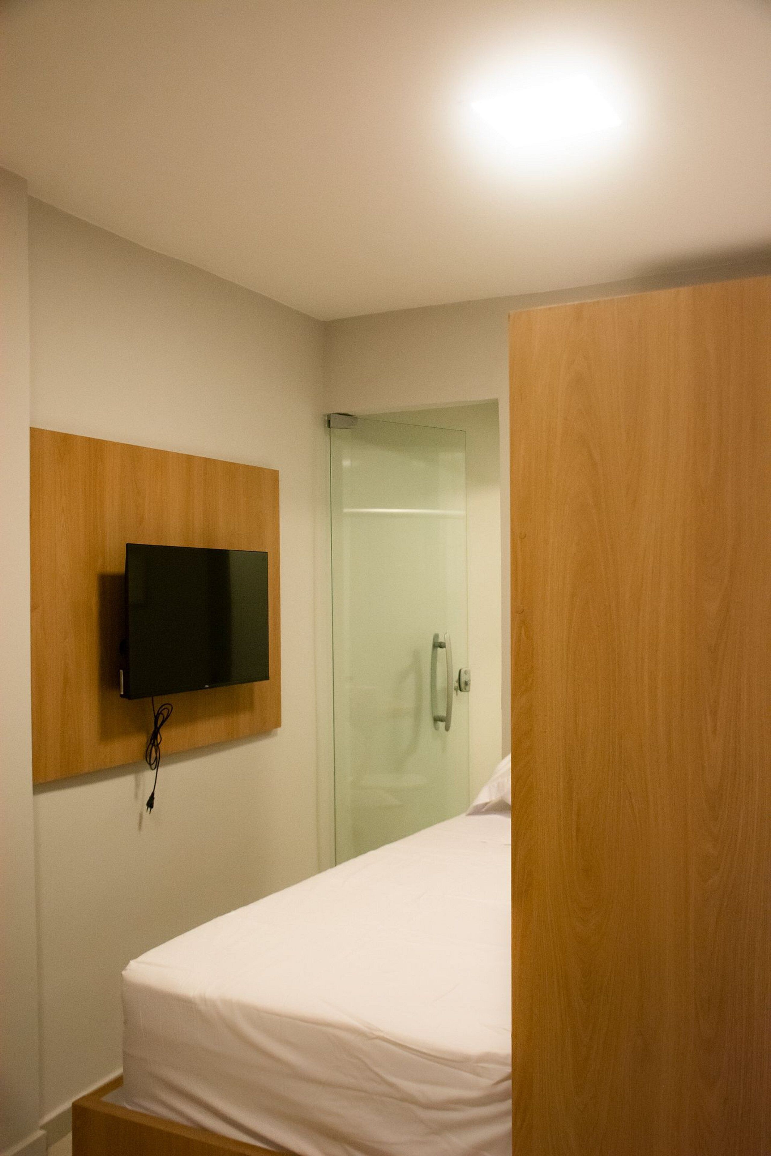 A hotel room with a bed, a mounted TV, and a glass shower door.