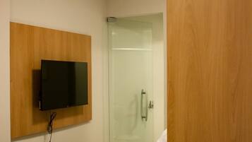 A hotel room with a bed, a mounted TV, and a glass shower door.