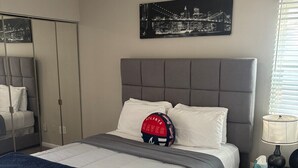 A bedroom with a bed, a nightstand, a lamp, a mirror, and a framed picture on the wall. - Cozy Sandy Springs Haven (Sandy Springs)