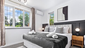 A modern bedroom with a large bed, a bedside table, a nightstand, and a window with curtains.