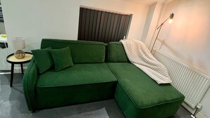 Ein modernes Wohnzimmer mit einem grünen Ecksofa, einem kleinen runden Tisch, einer Stehlampe und einer Heizung.