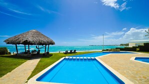 A pool area with a thatched gazebo, lounge chairs, and a view of the ocean. - Bright & Modern 2BR/2BA Apartment Comfort & Style In cabarete (Cabarete)