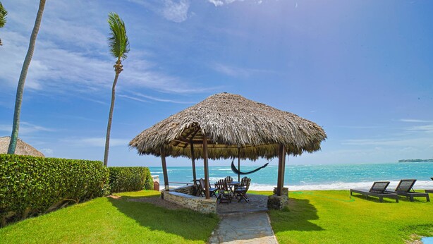 A thatched-roof gazebo with outdoor seating, a stone pathway, and a view of the ocean. - Bright & Modern 2BR/2BA Apartment Comfort & Style In cabarete (Cabarete)