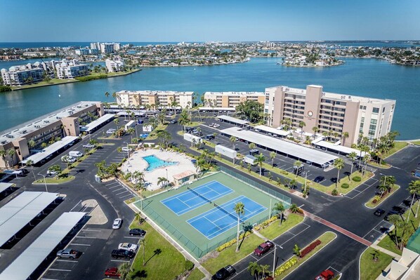 Un complexe hôtelier comprenant plusieurs bâtiments, une cour centrale avec une piscine, des courts de tennis et, au loin, une marina.