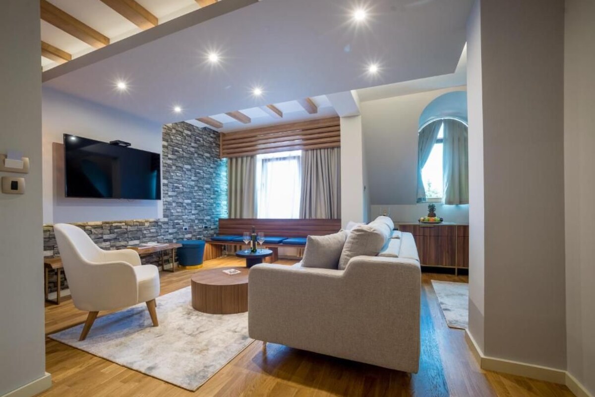 A modern living room with a stone accent wall, a flat-screen TV, a sofa, and a dining area with a wooden table and chairs.