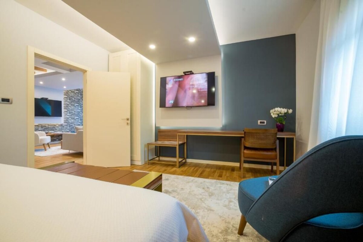 Een moderne hotelkamer met een bed, een bureau, een stoel en een aan de muur bevestigde televisie.