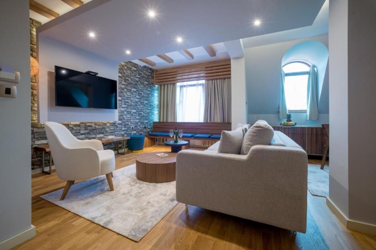 A modern living room with a stone accent wall, a flat-screen TV, a sofa, a coffee table, and a bench.