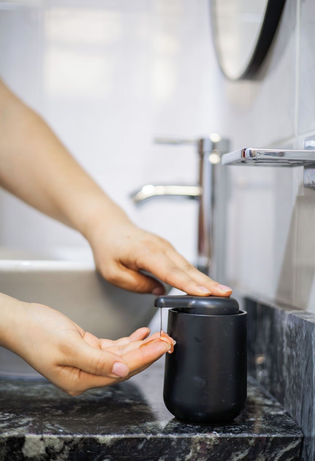 A hand holding a black mug under a faucet in a bathroom with a marble countertop.