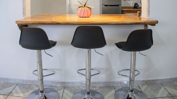 A kitchen with a wooden countertop, three black bar stools, and a vase with white flowers. - House with large kitchen, 1 block from third ring road (Aguascalientes)