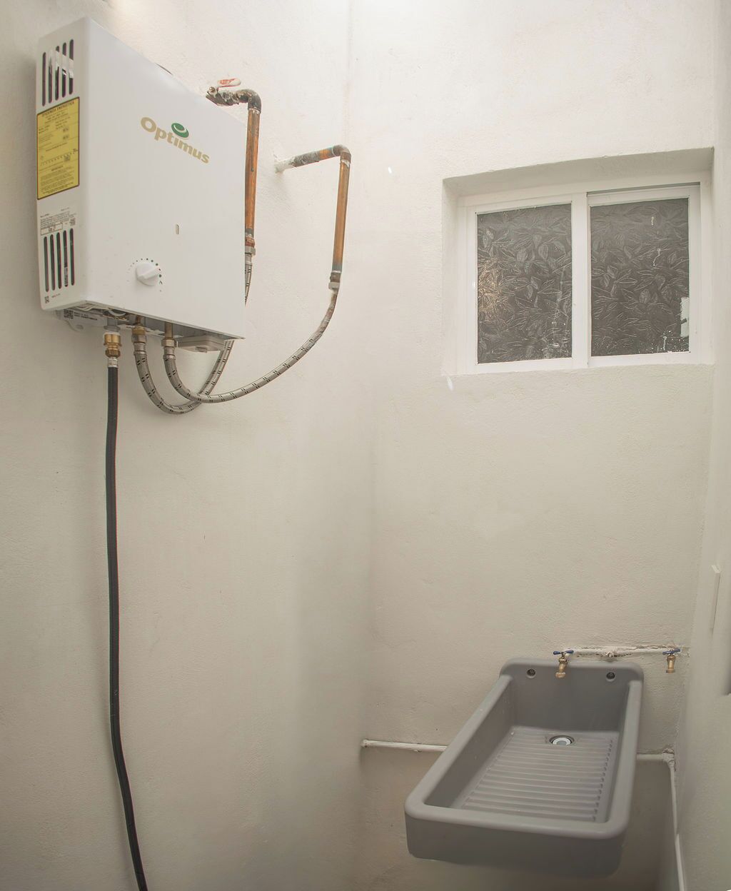 A small bathroom with a white wall, a window, and a shower unit labeled 'Optimus'.