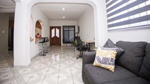 A modern living room with a grey sofa, a patterned throw pillow, and a dining area with a table and chairs. - House with large kitchen, 1 block from third ring road (Aguascalientes)