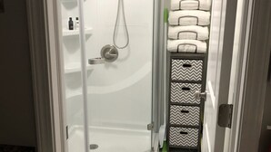 A bathroom with a glass-enclosed shower, a toilet, and a towel rack with neatly stacked towels.