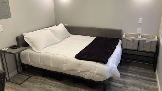 A bedroom with a bed, bedside tables, wall-mounted lights, a nightstand, and storage baskets.