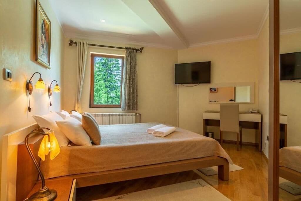 Una camera da letto con un letto, una scrivania, una sedia, una televisione e una finestra con tende.