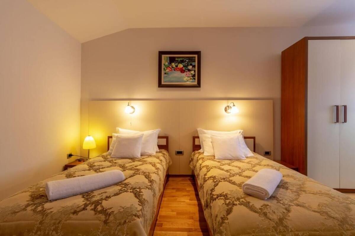 A hotel room with two beds, a wooden wardrobe, and a painting on the wall.