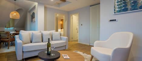 Una sala de estar moderna con sofá, sillón, mesa de centro y un comedor al fondo.