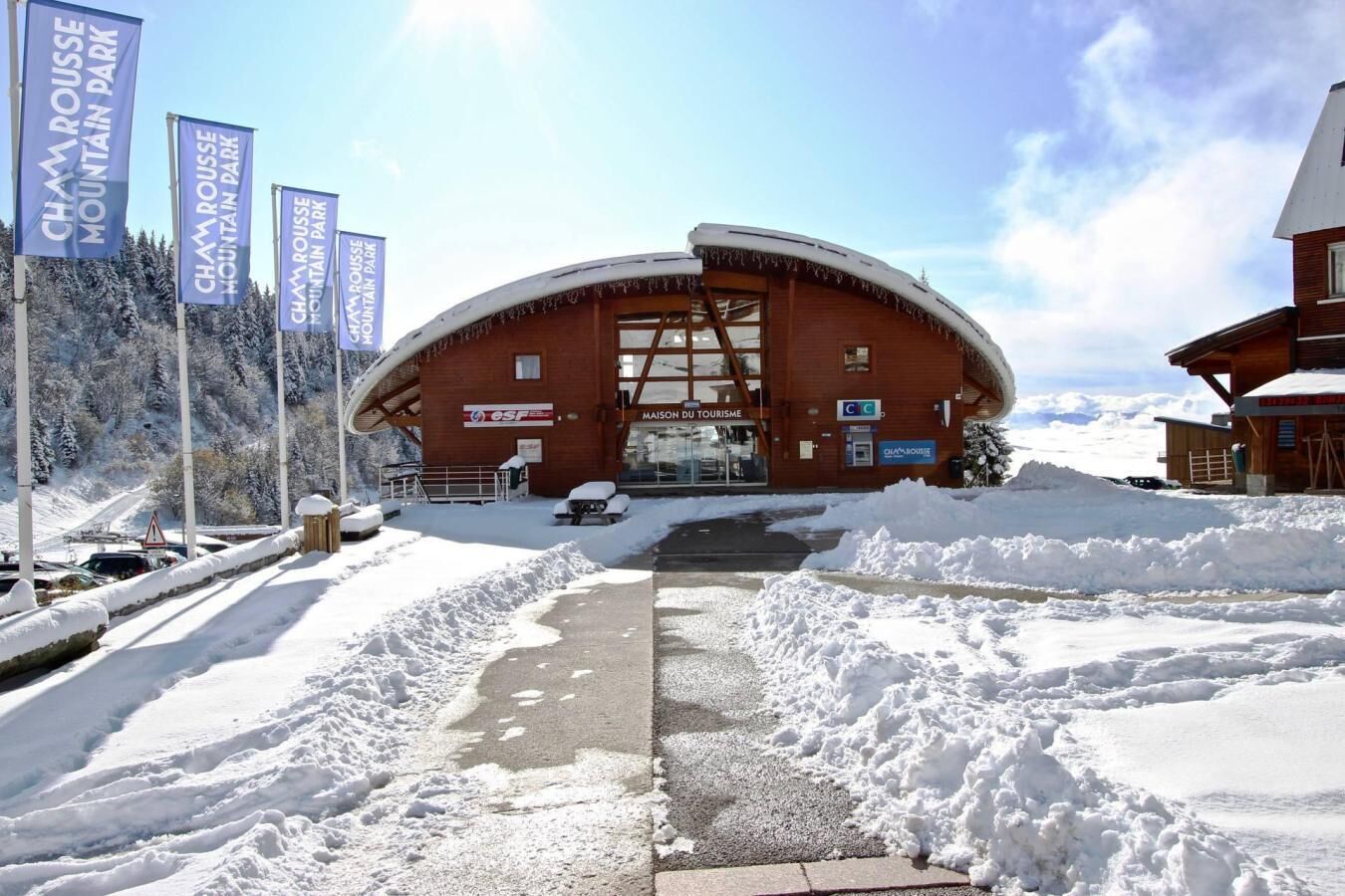 Un bâtiment enneigé avec un toit incurvé, une enseigne indiquant le parc de montagne de Chamrouse et une autre signalant la présence d’un office de tourisme.