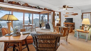 A cozy living room with a large window, a ceiling fan, and a fireplace. - Escape to the mountains in this cozy yet luxurious 3-bedroom, 2-bath retreat tucked away in the gated Bent Tree community of Jasper, GA! (Jasper)