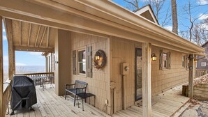 A wooden deck with a covered seating area, a grill, and a view of the landscape. - Escape to the mountains in this cozy yet luxurious 3-bedroom, 2-bath retreat tucked away in the gated Bent Tree community of Jasper, GA! (Jasper)