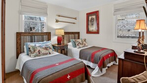 A hotel room with two beds, a wooden headboard, a nightstand with a lamp, a framed picture on the wall, and a window with a view of trees. - Escape to the mountains in this cozy yet luxurious 3-bedroom, 2-bath retreat tucked away in the gated Bent Tree community of Jasper, GA! (Jasper)