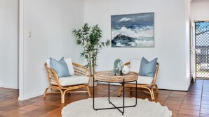 Ein Zimmer mit zwei Korbstühlen, einem runden Tisch und einem großen Gemälde einer Welle an der Wand.