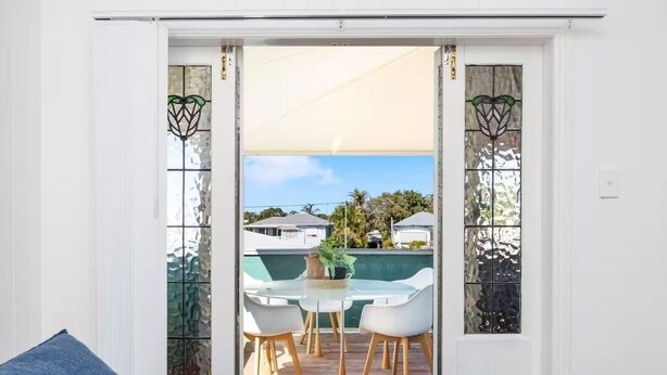 Ein Balkon mit Tisch und Stühlen, einem Blumentopf und Blick auf ein Schwimmbad und Gebäude.