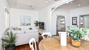Ein modernes Wohnzimmer mit grauem Sofa, weißen Sesseln, einem Holzes Esstisch und einem Fernseher.