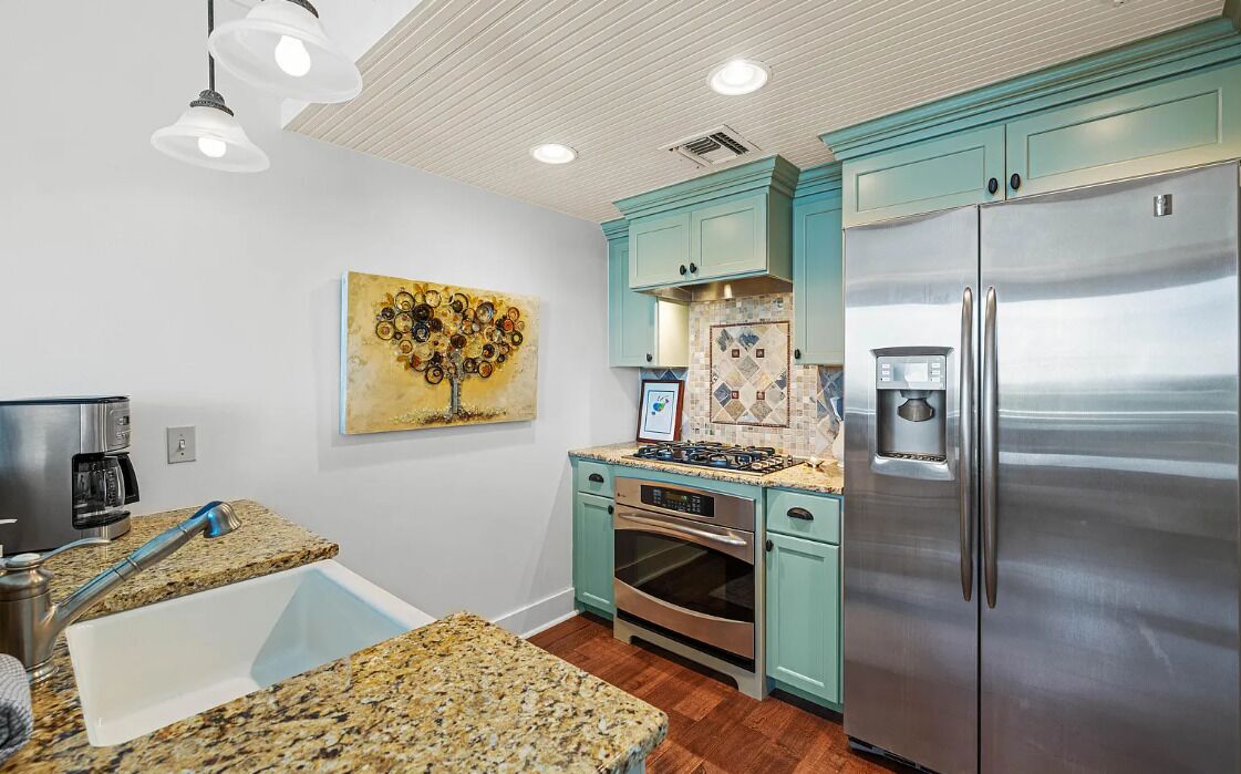 A modern kitchen with granite countertops, a stainless steel refrigerator, and teal cabinetry.