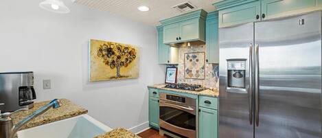 A modern kitchen with granite countertops, a stainless steel refrigerator, and teal cabinetry.