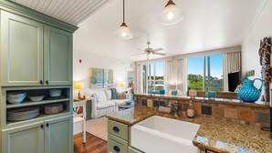 A modern kitchen with granite countertops, a built-in sink, and a dining area with a white table and chairs. - Salty's Six Palms 4A (Santa Rosa Beach)